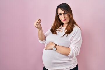 Fototapeta premium Pregnant woman standing over pink background doing italian gesture with hand and fingers confident expression