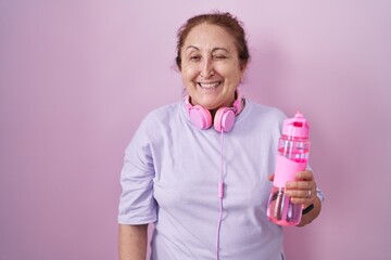 Senior woman wearing sportswear and headphones winking looking at the camera with sexy expression, cheerful and happy face.