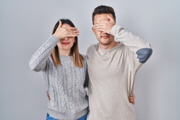 Young hispanic couple standing over white background smiling and laughing with hand on face covering eyes for surprise. blind concept.