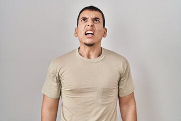 Young arab man wearing casual t shirt angry and mad screaming frustrated and furious, shouting with anger. rage and aggressive concept.