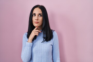 Hispanic woman standing over pink background thinking concentrated about doubt with finger on chin and looking up wondering