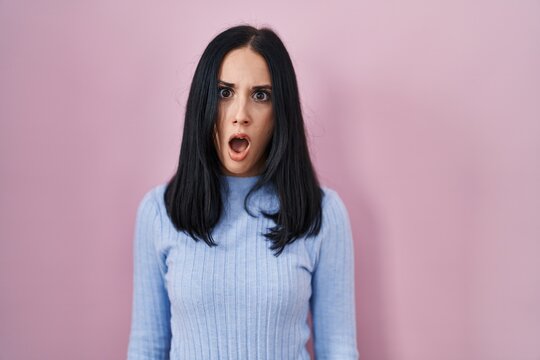 Hispanic woman standing over pink background in shock face, looking skeptical and sarcastic, surprised with open mouth