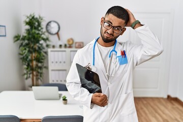 Young indian man wearing doctor uniform and stethoscope confuse and wondering about question....