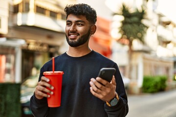 Young arab man using smartphone drinking soda at street