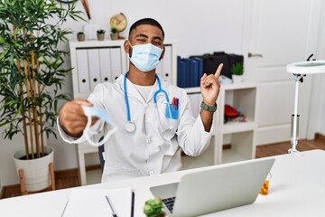 Young indian doctor offering safety mask smiling happy pointing with hand and finger to the side