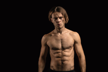 young sexy muscular man with a naked torso on a dark background. Long-haired man sportsman.