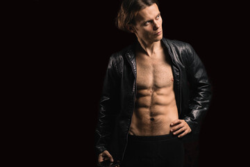 Fototapeta na wymiar handsome macho man with a naked torso in a black leather jacket on a dark background.