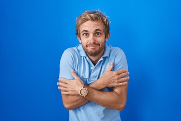 Caucasian man standing over blue background shaking and freezing for winter cold with sad and shock...