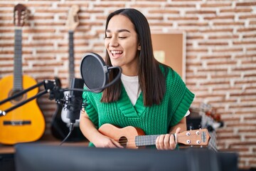 Fototapeta na wymiar Young hispanic woman musician singing song playing ukulele at music studio