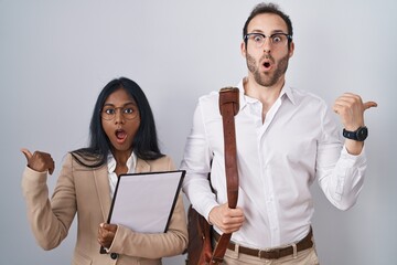 Interracial business couple wearing glasses surprised pointing with hand finger to the side, open mouth amazed expression.