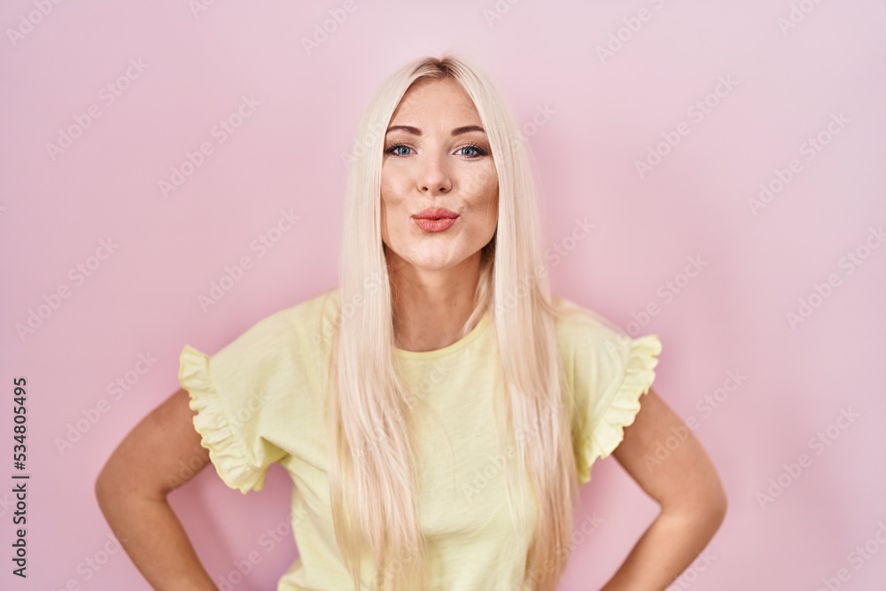 Wall mural caucasian woman standing over pink background looking at the camera blowing a kiss on air being love