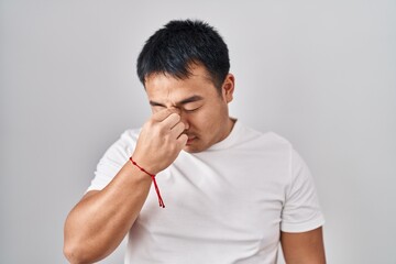 Young chinese man standing over white background tired rubbing nose and eyes feeling fatigue and headache. stress and frustration concept.
