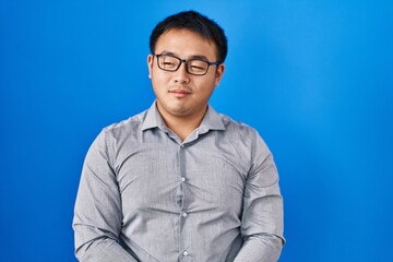 Young chinese man standing over blue background smiling looking to the side and staring away thinking.