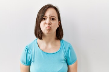 Young down syndrome woman standing over isolated background puffing cheeks with funny face. mouth inflated with air, crazy expression.