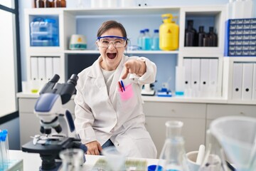 Hispanic girl with down syndrome working at scientist laboratory pointing displeased and frustrated...