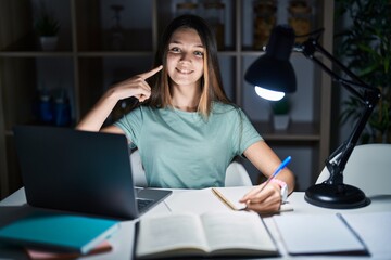 Teenager girl doing homework at home late at night smiling cheerful showing and pointing with fingers teeth and mouth. dental health concept.