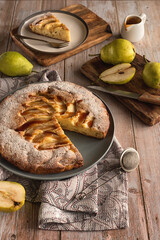 Autumn baking: homemade pear pie and ripe pears on a light wooden table. Open pie with pears and caramel. Photo in rustic style.