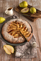 Autumn baking: homemade pear pie and ripe pears on a light wooden table. Open pie with pears and caramel. Photo in rustic style.