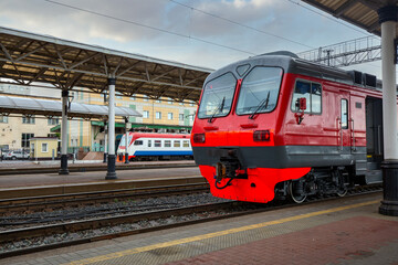 A bright red train stands on the platform of the railway station in the city. Passenger Transportation.