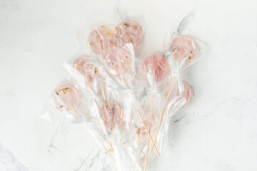 Confectioner's hand holding pink homemade caramel lollipops with wooden sticks
