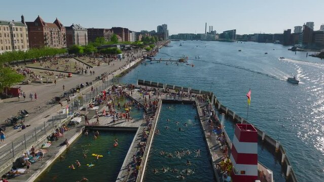 Forwards fly along waterfront. People relaxing at water, enjoying hot sunny day in city. Swimming and riding kayak. Copenhagen, Denmark