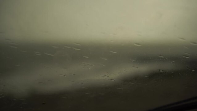 Raindrops falling on a car window with wipers on