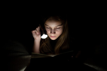 A teenage girl reads in the dark with a flashlight.
