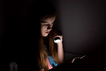 A teenage girl reads in the dark with a flashlight.