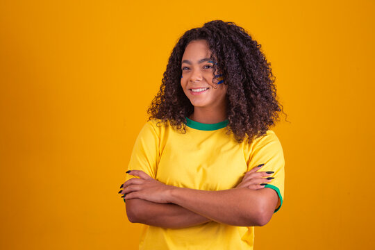Young black Brazilian, soccer fan. arms crossed over the body. Beautiful brazilian cheerleader with arms crossed on yellow background