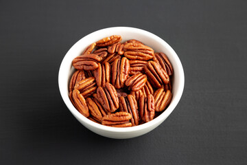 Homemade Shelled Pecans in a bowl on a black background, side view.