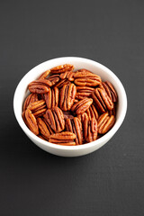 Homemade Shelled Pecans in a bowl on a black background, side view.