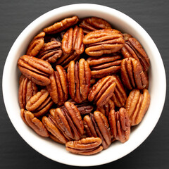 Homemade Shelled Pecans in a bowl on a black background, top view. Flat lay, overhead, from above.