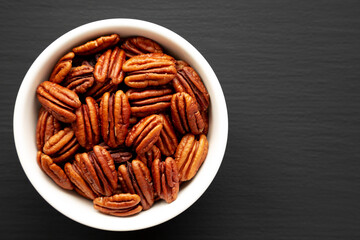 Homemade Shelled Pecans in a bowl on a black surface, top view. Flat lay, overhead, from above. Copy space.