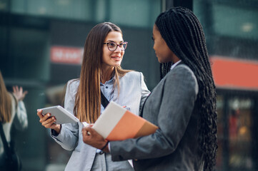 Two multiracial business woman meeting outside and using a tablet