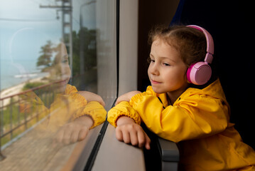 A girl in headphones on a train looks out the window. Journey.