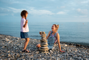 A mother and daughter 6 years old on the beach build a castle of stones. They socialize and have fun together. Family. Summer. Vacation.