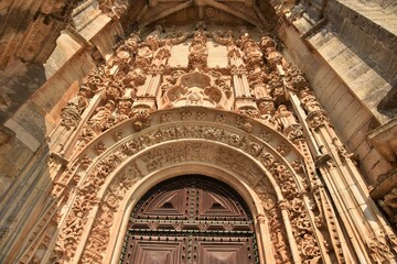 Fototapeta premium Cream color Manueline sandstone entrance to Convent of Christ rotunda church, Mary and Child and 12 apostles towering adornments of acanthus, putti, intertwined ropes, gargoyles, in Tomar, Portugal