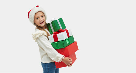 Christmas child. Cute toddler girl in santa claus hat holding high stack of colorful gift boxes on white background
