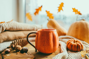 A cup of hot steaming tea and a pumpkin-shaped candle on the windowsill, autumn mood