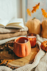 A cup of tea in the shape of a pumpkin against the background of stacks of sweaters, autumn mood