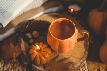 Burning candle pumpkin and a cup of tea on the background of a stack of sweaters, autumn composition