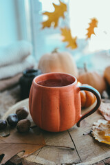A cup of hot steaming tea and a pumpkin-shaped candle on the windowsill, autumn mood