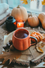 A cup of hot steaming tea and a pumpkin-shaped candle on the windowsill, autumn mood