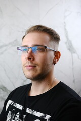 Male beauty concept. Portrait of fashionable young man with stylish haircut wearing trendy glasses and tshirt, posing over gray background. Perfect hair. Copy-space. Studio shot