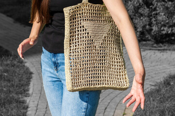 Fashionable emotional woman wearing in t-shirt and jeans with handmade crocheted knitting bag, made...