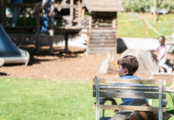 bored little boy looking away while kids enjoy the playground.