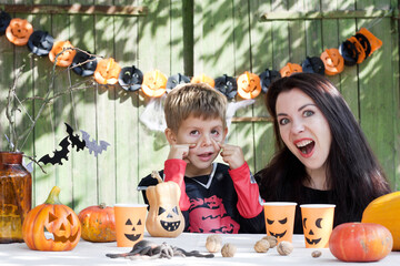 Portrait of mother and son in Halloween costumes sitting at table background of old wooden wall. young woman and child are having fun celebrating Halloween, grimacing, mouth wide open