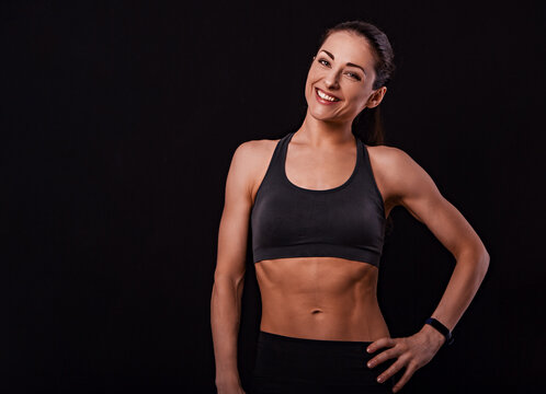 Smiling fit healthy fitness woman in bra top clothing looking happy with sporty watches on the hand on black background with empty copy space. Closeup