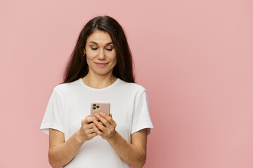 horizontal portrait of a woman in a white t-shirt standing on a pink background with a phone in her hands