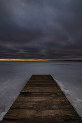 old boardwalk pier on a frozen lake under a cloudy sky. gloomy winter landscape